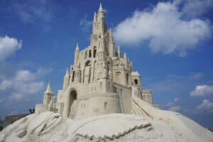 Sandcastle building is one of the fun activities you can do in South Padre. This image features a large and intricate sand castle on the beach with a blue sky with clouds in the background.