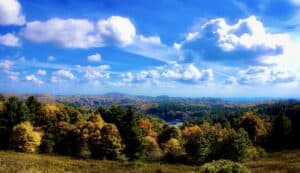 This image features a lovely fall landscape of multi-colored trees with a bright blue sky and large white fluffy clouds above.