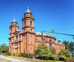 This image features the Basilica of Saint Lawrence in Asheville, North Carolina. It is a beautiful red brick church with Twin steeples on the front and a domed central area of the church behind
