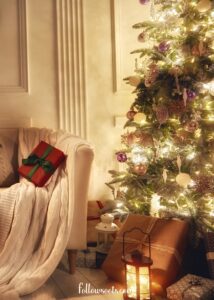 This image features  cozy holiday scene with a brightly lit Christmas tree on the right and a chair draped with a blanket with a red wrapped present on top. - Cheap Christmas Tree Decorating Ideas