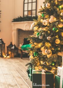 This image features an elegant room with a fireplace in the background and a green cushion and a Christmas tree in the foreground decorated with green and gold balls. 