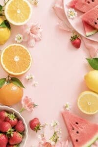This wallpaper image features a light pink background with fruits lined on the left and right of the wallpaper. Fruits included are watermelons, lemons, oranges and strawberries. 