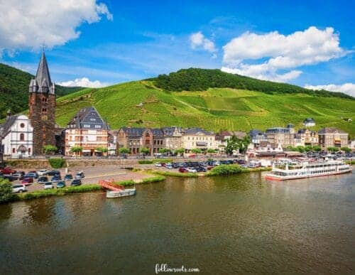 Pretty Places in Germany - Bernkastell-Kues. This image features a cute historic German village overlooking the Moselle River with a river cruise boat on the water by the town.