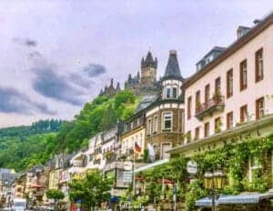 This image features the historic village of Cochem, Germany located along the Mosell River, with Cochem Castle sitting on the hill above thee town.