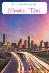 This Pinterest Pin image features a sunset view of the Houston, Texas Skyline with light trail streaks on the freeway in the foreground and a row of tall buildings in the background with a sunset sky.
