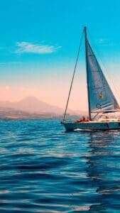 Thia image features a sailboat on the water with a mountain sunset in the background