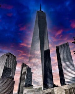 This image features the Freedom Tower in New York City surrounded by other buildings with a striking sunset in the background - Beautiful Travel Aesthetic Wallpapers