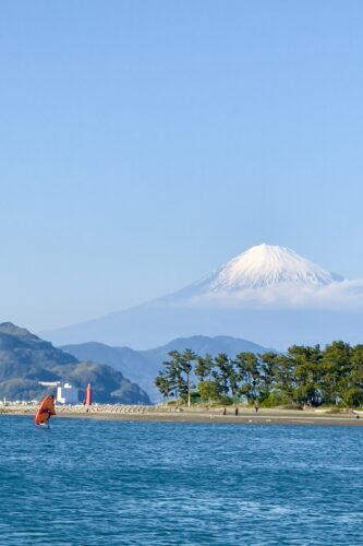 This image features a beautiful clear day with a view of Mount Fuji in the background under a bright blue sky with a windsurfer on the water in the foreground.- Beautiful Travel Aesthetic Wallpapers