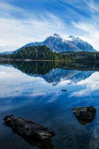 This image features a large snowcapped mountain with a lake in the foreground which is reflecting the mountain. It is in Bariloche, Argentina. - Beautiful Travel Aesthetic Wallpapers