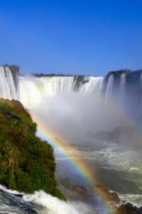 This image features the large and impressive Iquazu Falls, with a rainbow in the foreground. They are located in  Argentina