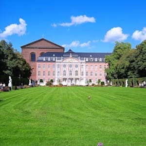A stunning view of the Baroque Electoral Palace in Trier, Germany, with lush gardens under a clear blue sky.