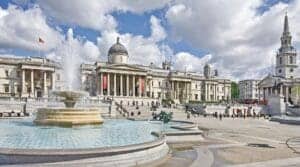 This image features Trafalgar Square in London with a lovely picturesque blue sky with clouds above.