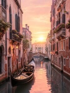 7 Dreamy European Destinations - This image features a Venice canal at sunset. There is a gondola floating in the canal between two building and the sun is setting in the background.