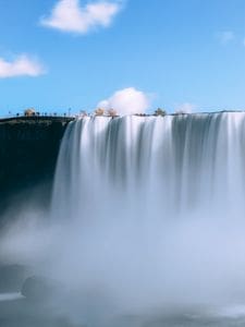 Capture of Niagara Falls with a blue sky backdrop, showcasing its majestic flow and misty ambiance.