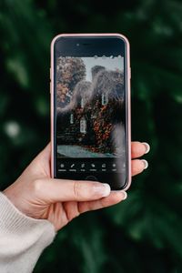 Close-up of a hand holding a smartphone showing a nature scene on the screen.