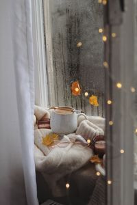 Warm cozy scene with coffee, glasses, and autumn leaves by a rainy window.