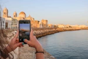 Woman photographing beautiful Cadiz waterfront scene with smartphone during golden hour. - How to take better photos with your phone