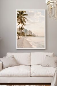 This image features a calm and muted beach scene with tall palms trees swaying in the wind on the beach with high rise buildings in the background.